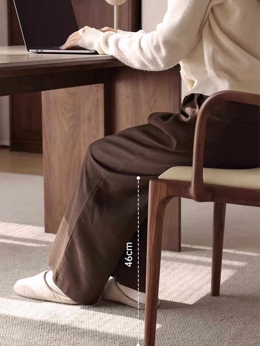 Side profile of the Cael dining arm chair showing the sculptural walnut frame and cream seat cushion.