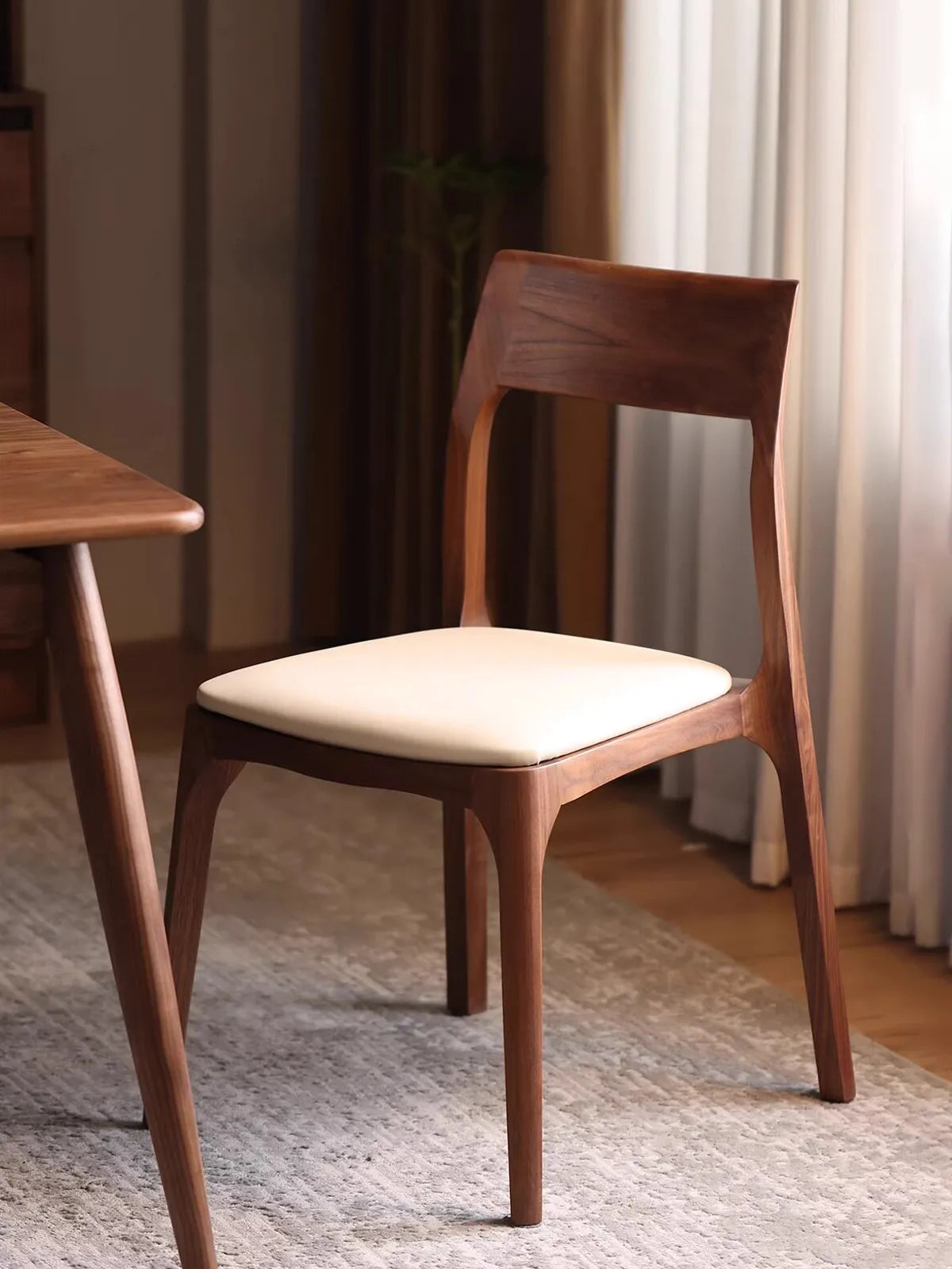 Angled view of the contemporary walnut dining chairs showcasing its minimalist design, rich wood grain, and comfortable cream-colored padded seat cushion.