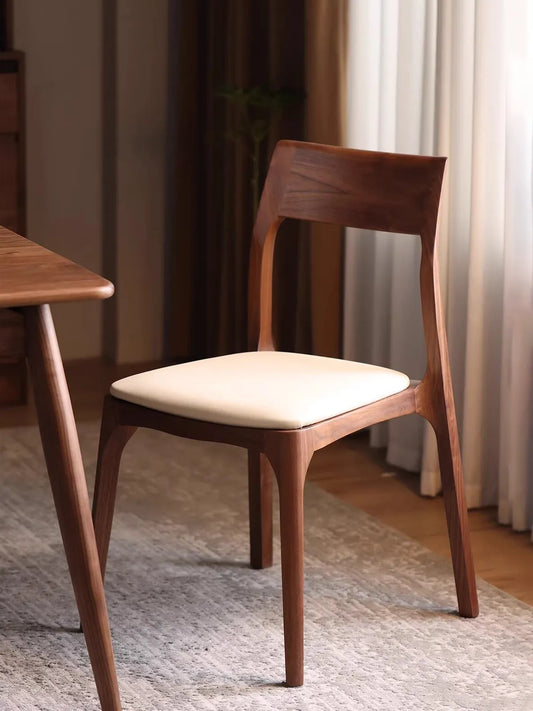 Angled view of the contemporary walnut dining chairs showcasing its minimalist design, rich wood grain, and comfortable cream-colored padded seat cushion.