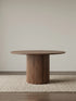 Front view of a solid American black walnut round pedestal dining table with a fluted pillar base and softly beveled top.