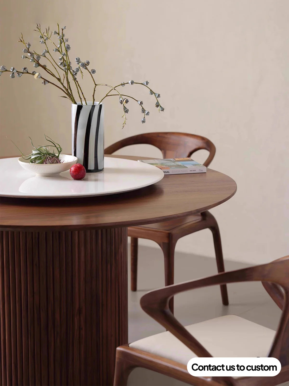 Close view of the walnut round dining table with fluted pedestal, white lazy Susan, vase, and surrounding chairs.