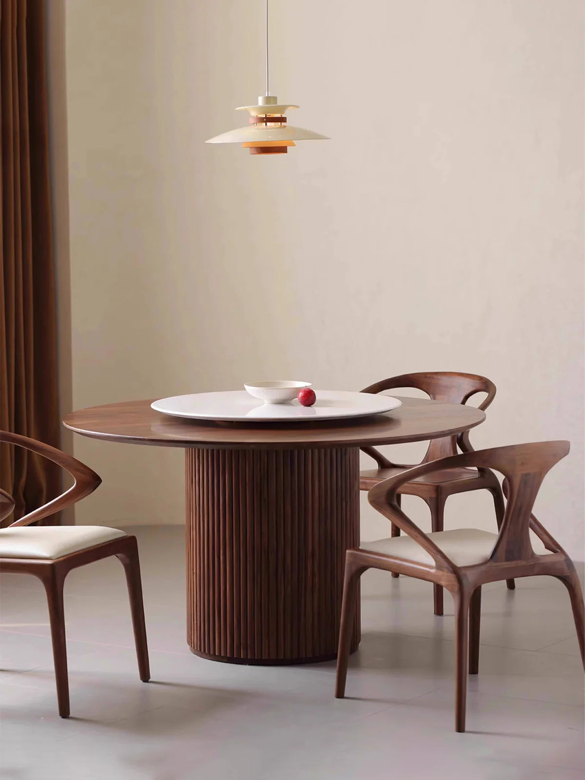 Full room view of a round pedestal dining table in walnut with three sculptural chairs and a white rotating center tray.
