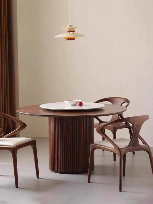 Full room view of a round pedestal dining table in walnut with three sculptural chairs and a white rotating center tray.