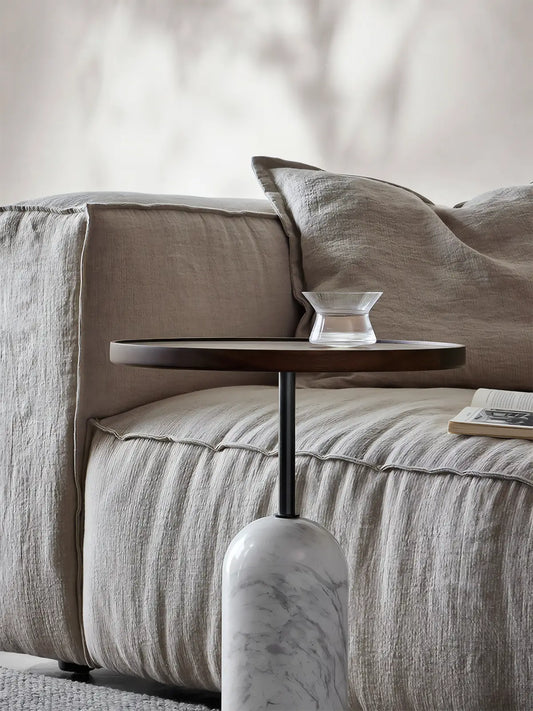 Solid black walnut side table styled next to a linen sofa in a modern living room, showing pedestal design.