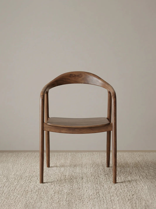 front view of a curved back walnut dining chair with wraparound backrest and sculpted seat