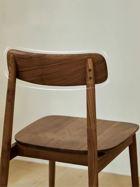 Rear three-quarter view of a solid walnut dining chair highlighting the softly curved low backrest, tapered rear legs, and open back profile.