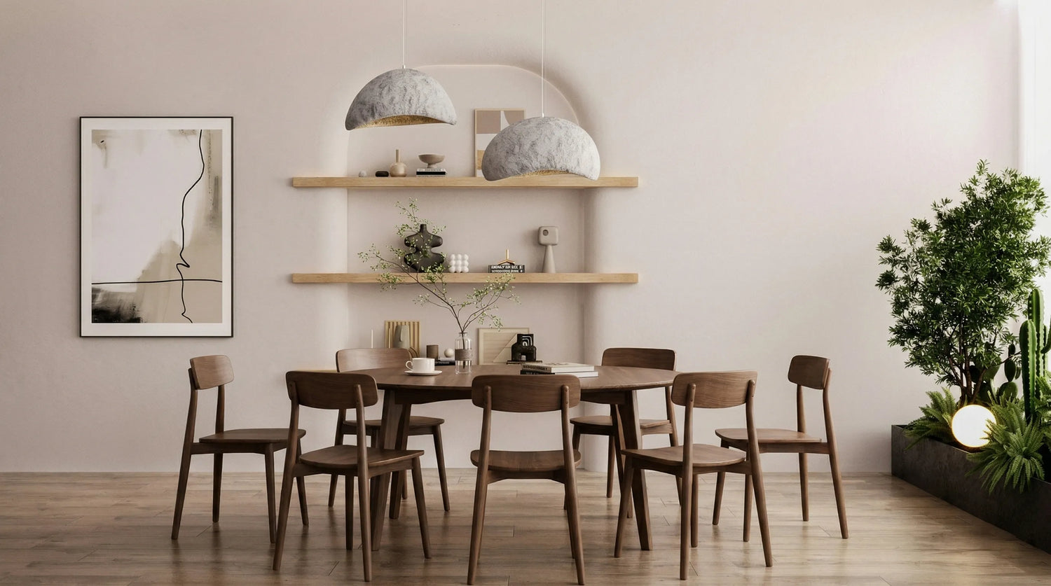 Angled lifestyle view of a round walnut dining table for four with a sculptural base in a softly lit modern dining room.