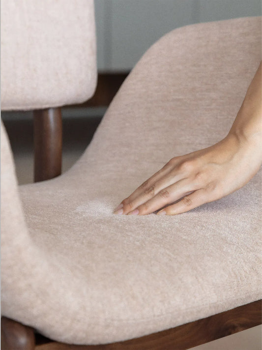 Close-up of textured beige upholstery on a walnut dining chair with a hand pressing into the cushioned seat