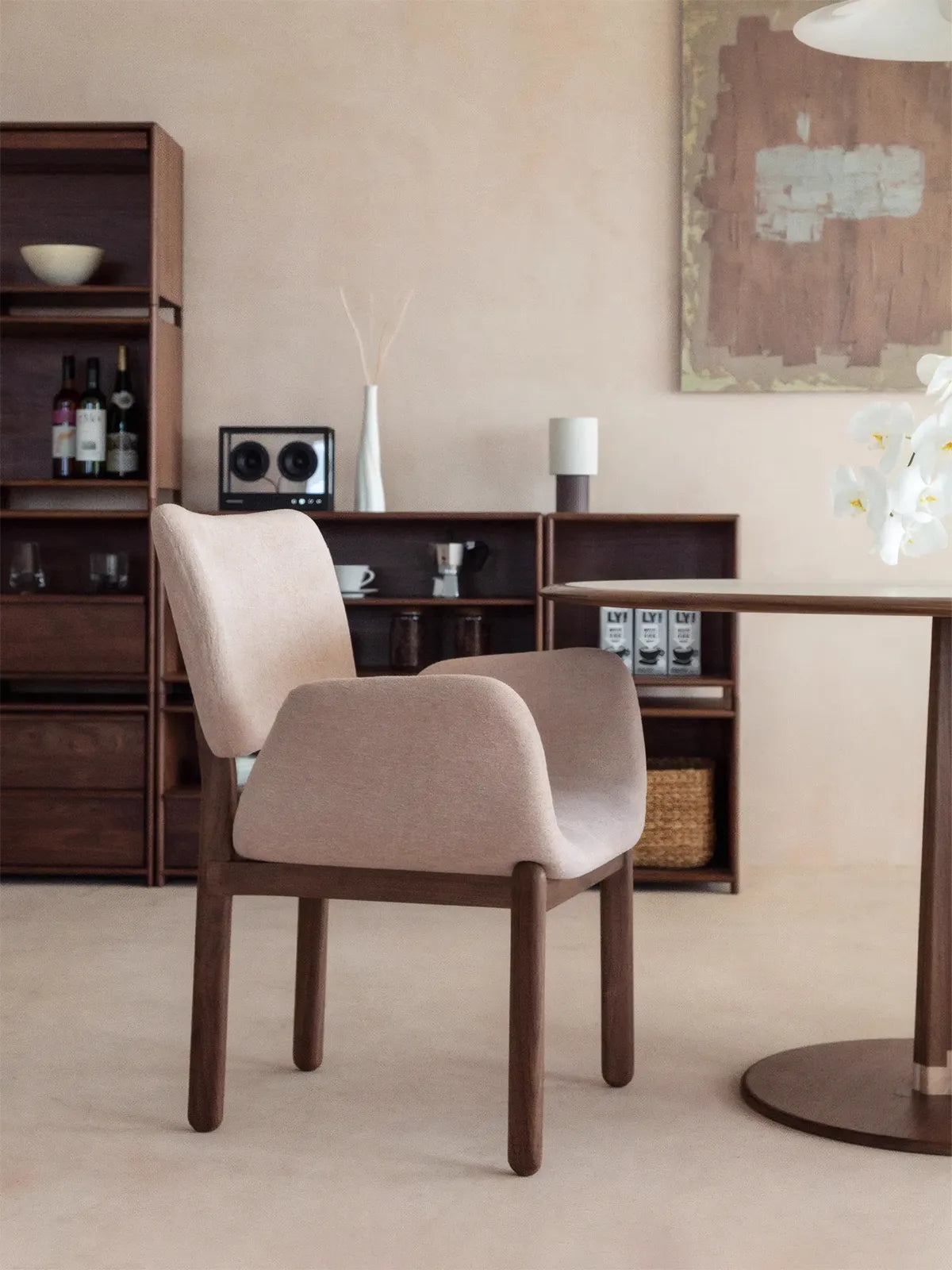 Beige upholstered walnut dining arm chair shown beside a round dining table in a warm minimalist interior