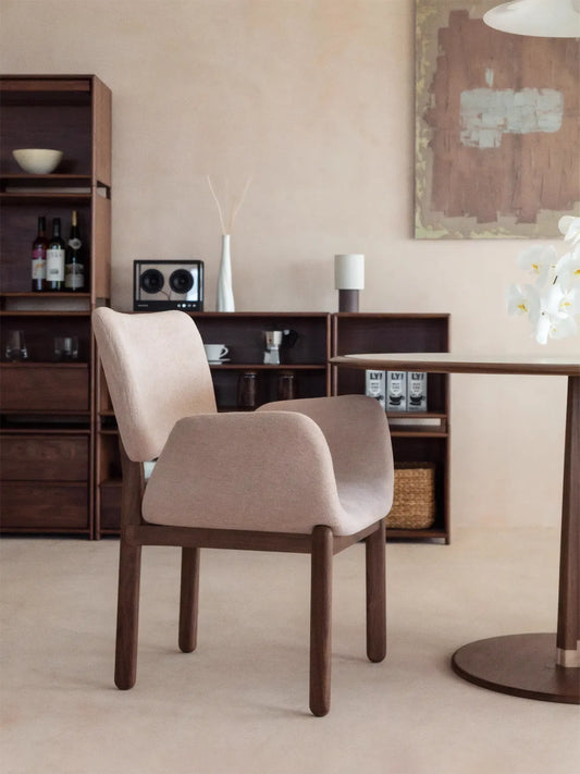 Beige upholstered walnut dining arm chair shown beside a round dining table in a warm minimalist interior
