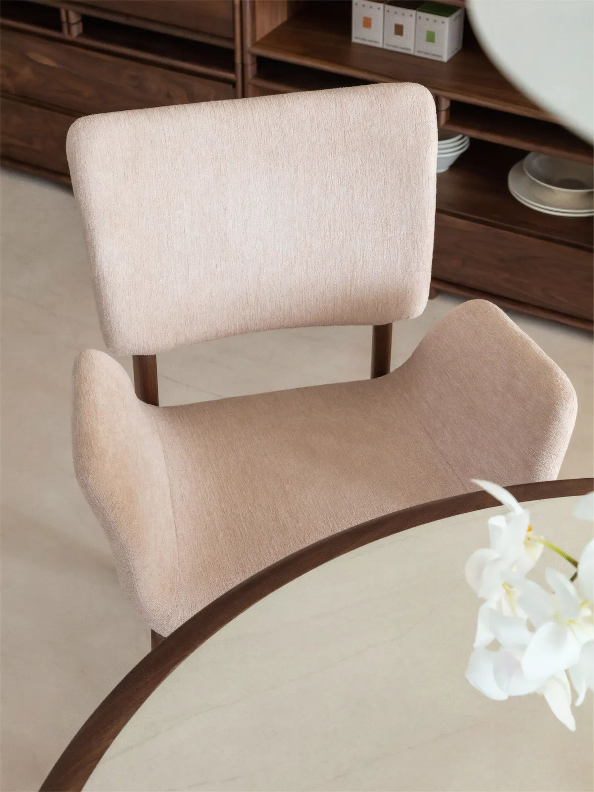 Overhead detail of a beige upholstered dining chair with arms showing the curved seat form and floating backrest