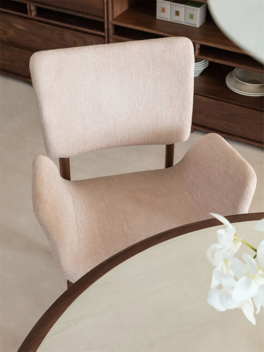 Overhead detail of a beige upholstered dining chair with arms showing the curved seat form and floating backrest