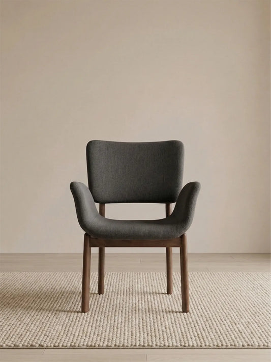 Front view of a charcoal upholstered walnut dining chair with arms on a textured neutral rug (Obsidian)