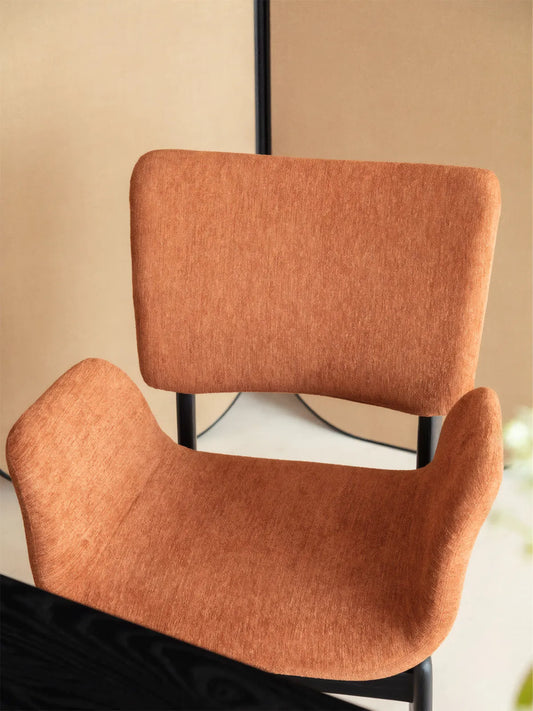 Front detail of a rust upholstered dining armchair with a softly curved back and sculpted arms