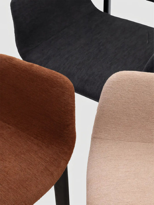 Close-up comparison of upholstered dining armchair color options in rust, black, and beige