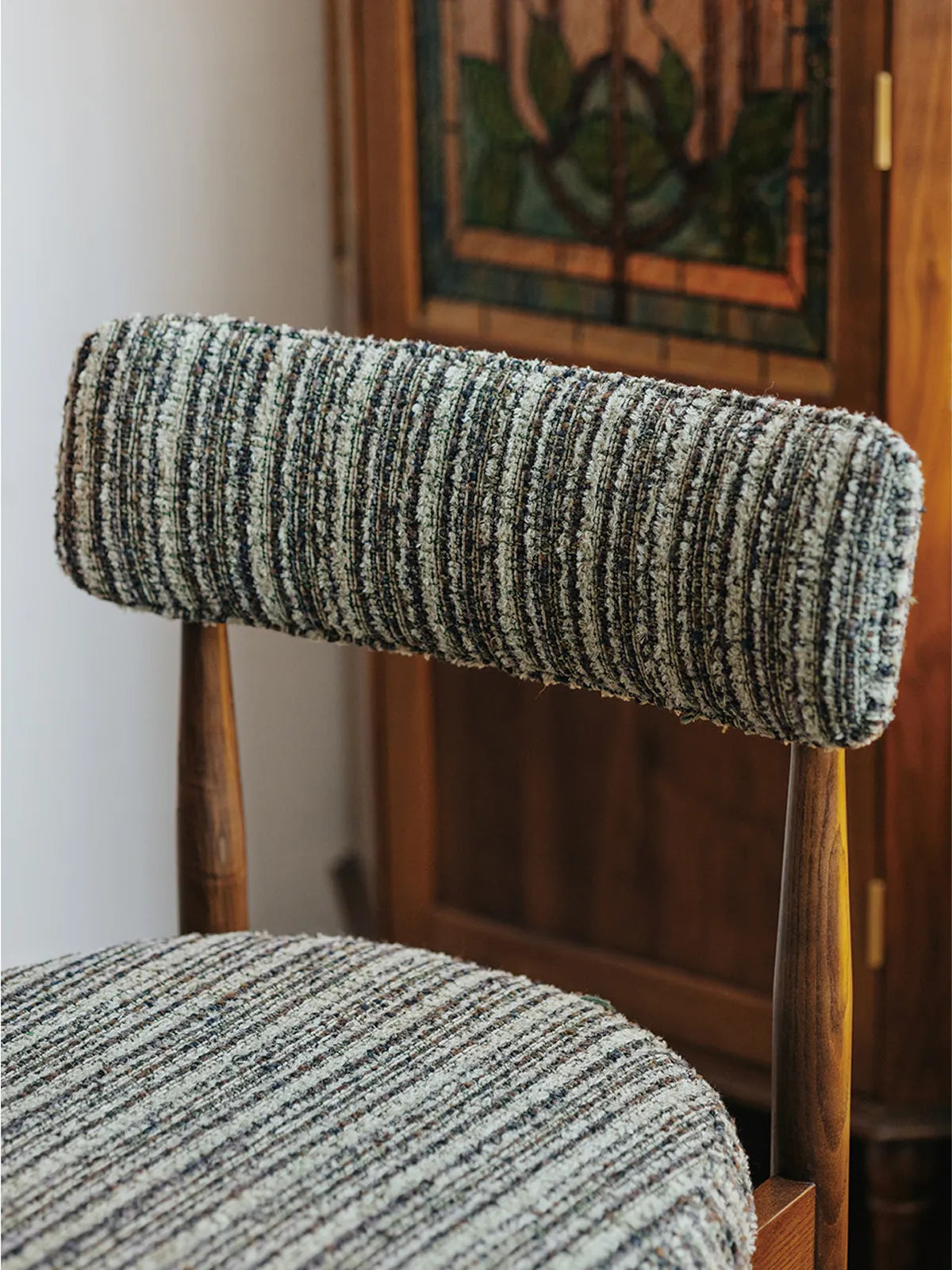 Detail of the Eron dining chair curved padded backrest in textured bouclé fabric with walnut frame visible behind