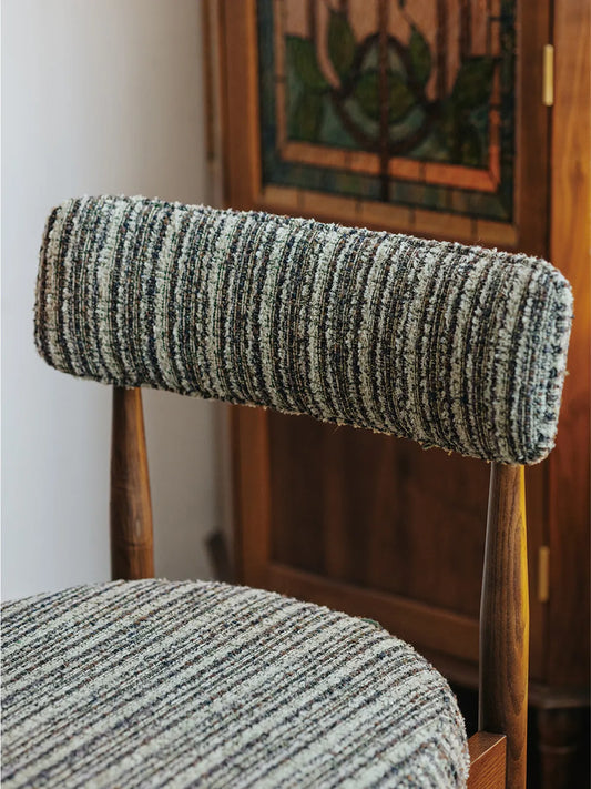 Detail of the Eron dining chair curved padded backrest in textured bouclé fabric with walnut frame visible behind