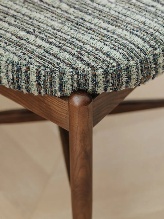Close-up of walnut leg joint and seat frame corner on the Eron dining chair showing turned wood detail and fabric edge
