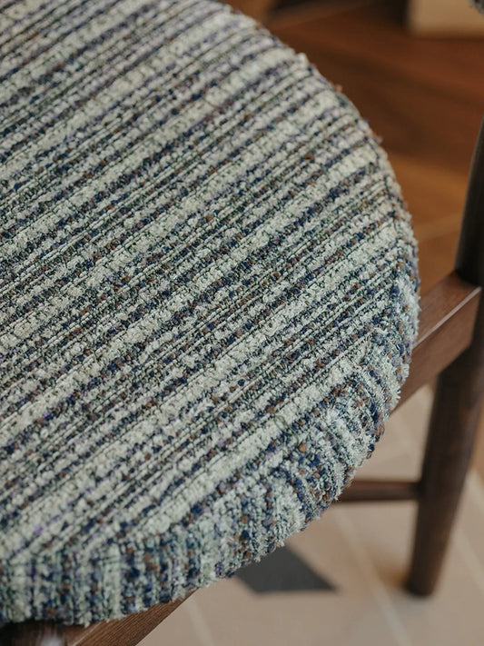 Close-up of the Eron dining chair rounded seat cushion showing green and cream bouclé-textured woven fabric