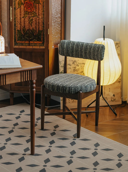 Eron dining chair rear three-quarter view in styled room showing walnut back posts and padded backrest