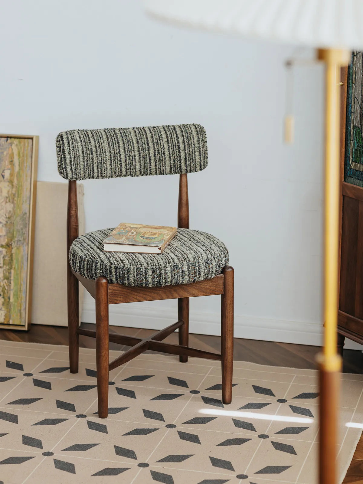 Eron walnut dining chair styled on patterned tile floor with books on the seat, three-quarter front angle