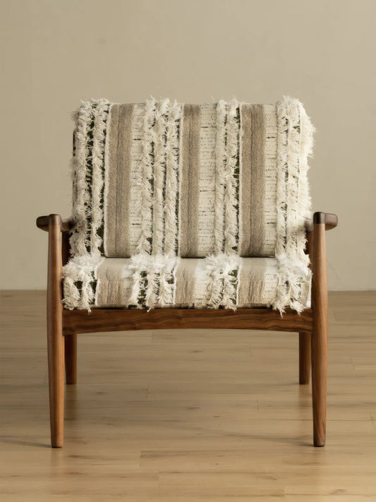 Eron walnut lounge chair front view on light wood floor, showing full frame and fringed woven cushions