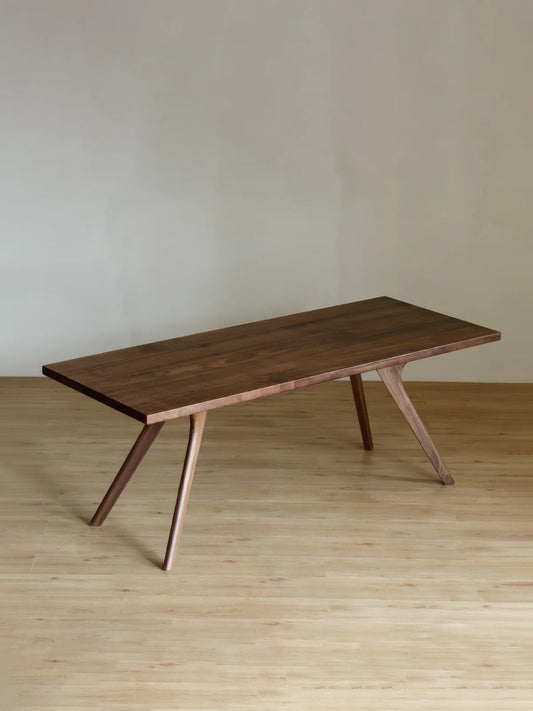 Angled view of the Estate solid walnut dining table showing its slim top and splayed leg structure.