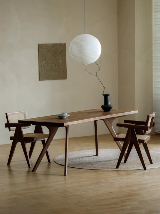 Full room view of the Estate mid-century modern walnut dining table with two matching chairs, a paper pendant light, and a round natural rug.