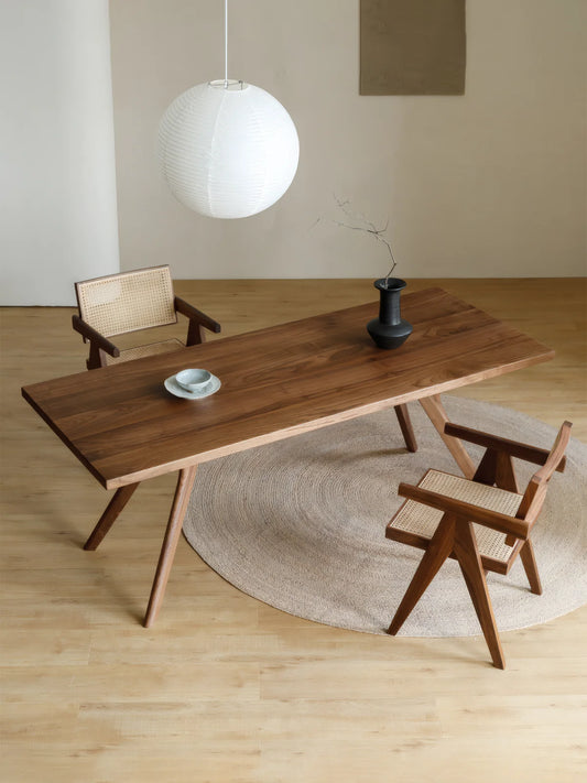 Overhead room view of the Estate solid walnut dining table with sculpted legs and two coordinating walnut and cane chairs.