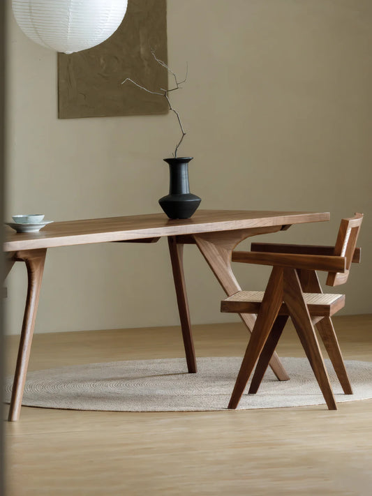 Side view of the Estate solid walnut rectangular dining table with sculpted angled legs, a black vase, and a matching walnut chair.