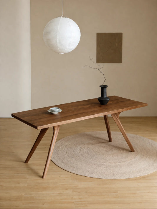 Side angled view of the Estate dark walnut dining table with a tapered top, black vase, and soft neutral styling.