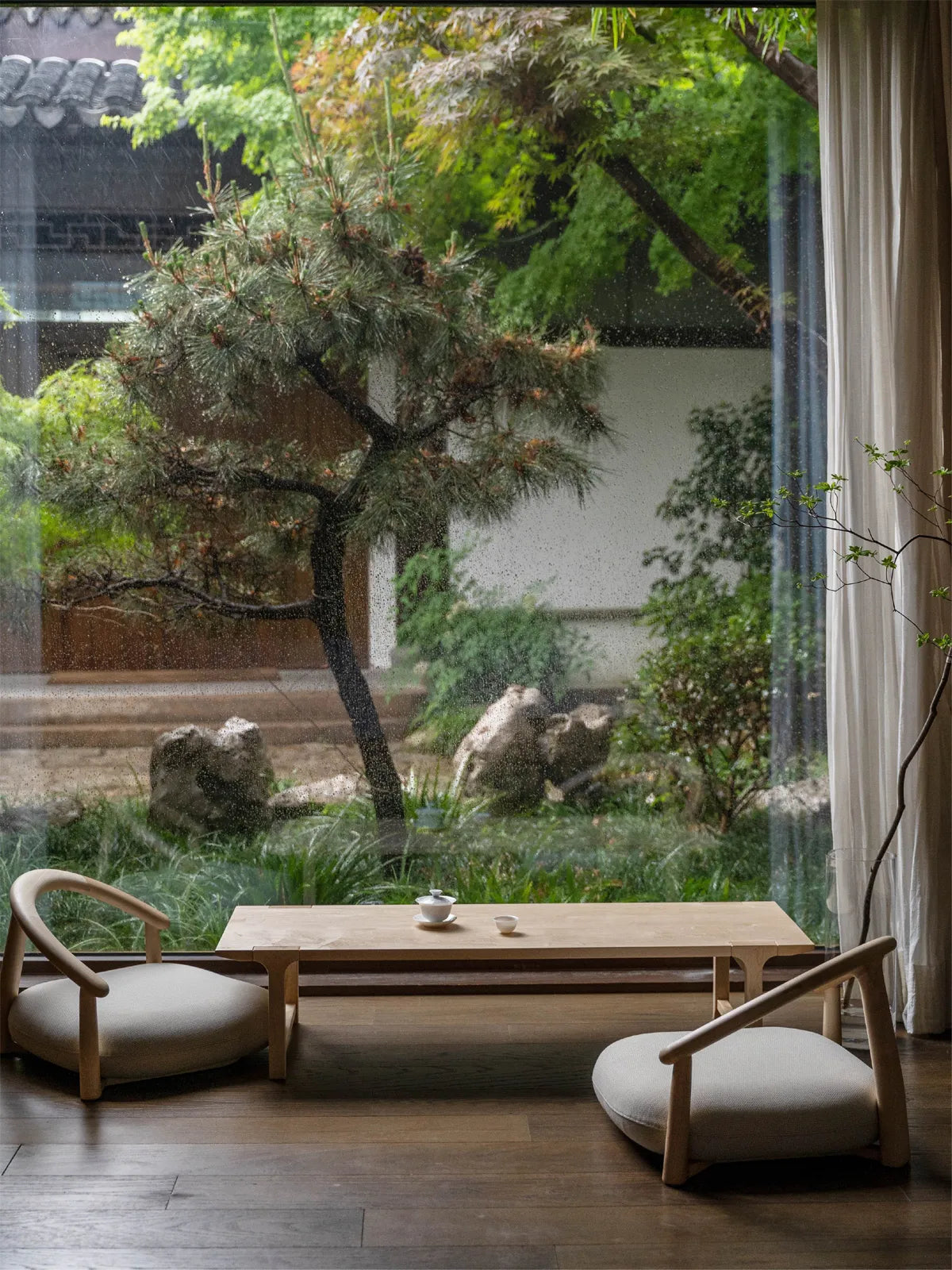 A relaxing Japandi-style tea room setup featuring two Haven Wide-Seat Floor Chairs and a matching low wooden table against a scenic rainy window.