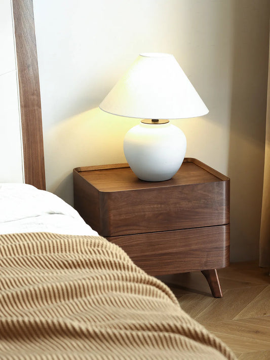 Angled view of The Helios 2-drawer walnut nightstand, showcasing its mid-century modern design, splayed legs, and smooth curved corners.