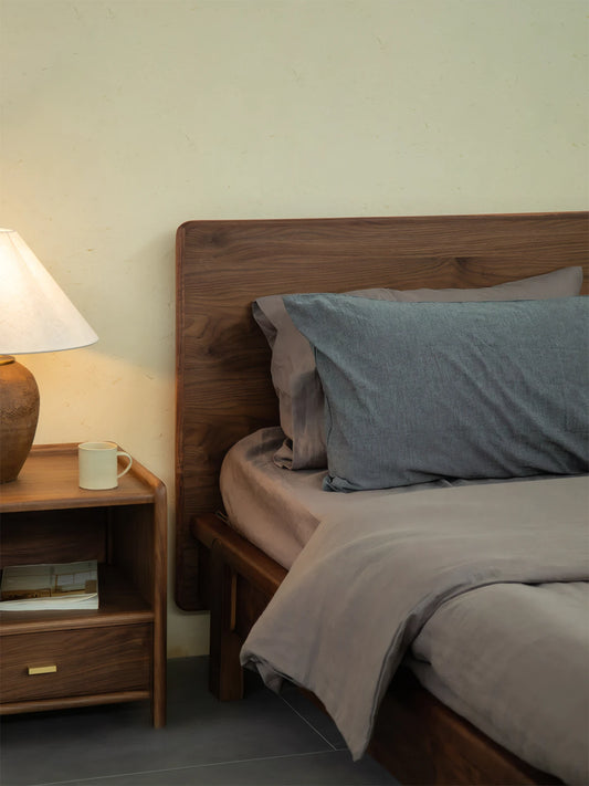 Detail shot of the smooth, continuous wood grain on the solid walnut headboard of The Helios Bed Frame, styled with cozy gray bedding.