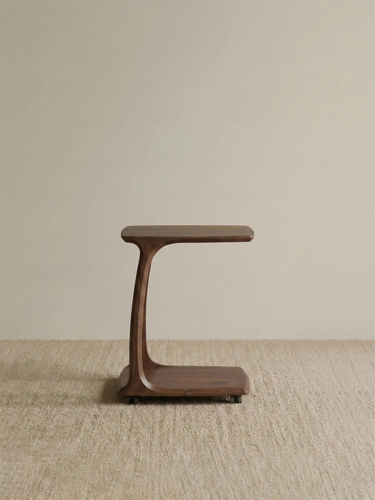 Side profile of The Helios solid wood C-Table in a studio setting, highlighting its elegant curved structure and convenient hidden caster wheels.