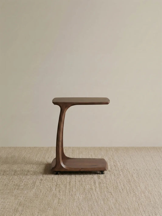 Side profile of The Helios solid wood C-Table in a studio setting, highlighting its elegant curved structure and convenient hidden caster wheels.