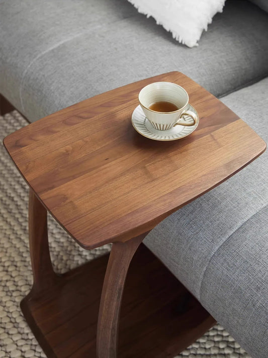 Top view of The Helios solid walnut C-table resting over a sofa cushion, featuring a teacup and showcasing the beautiful natural continuous wood grain.