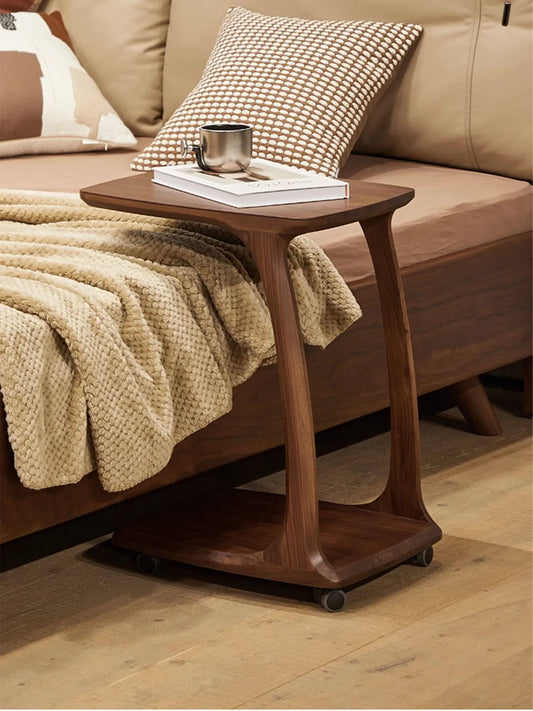 The versatile Helios C-table with wheels easily sliding under a solid wood bed frame, serving as a functional bedside laptop or coffee table.