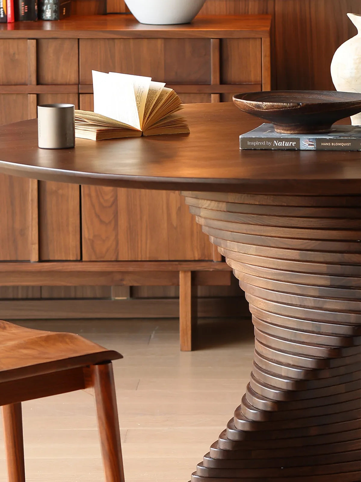 Macro shot highlighting the smooth solid walnut table edge and the top tiers of the sculptural pedestal base on The Helios Round Dining Table.
