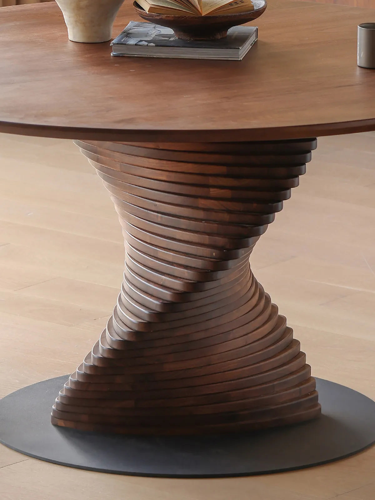 Close-up architectural detail of the unique twisted slatted wood pedestal base on The Helios Round Dining Table, crafted from solid North American Black Walnut.