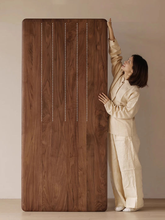 A woman standing next to the Helios table placed vertically, demonstrating its impressive length and premium solid wood planks.