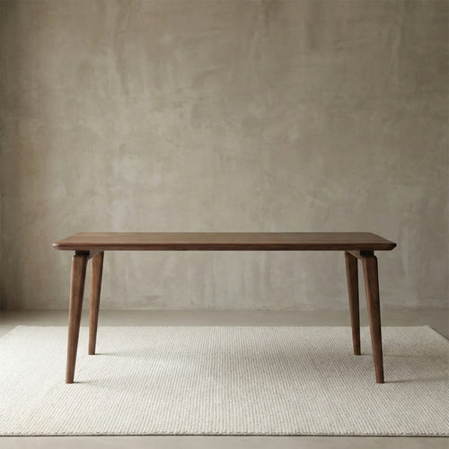 Front view of the standalone Walnutry Helios dining table against a textured wall, showcasing its sleek tapered legs and elegant mid-century modern silhouette.