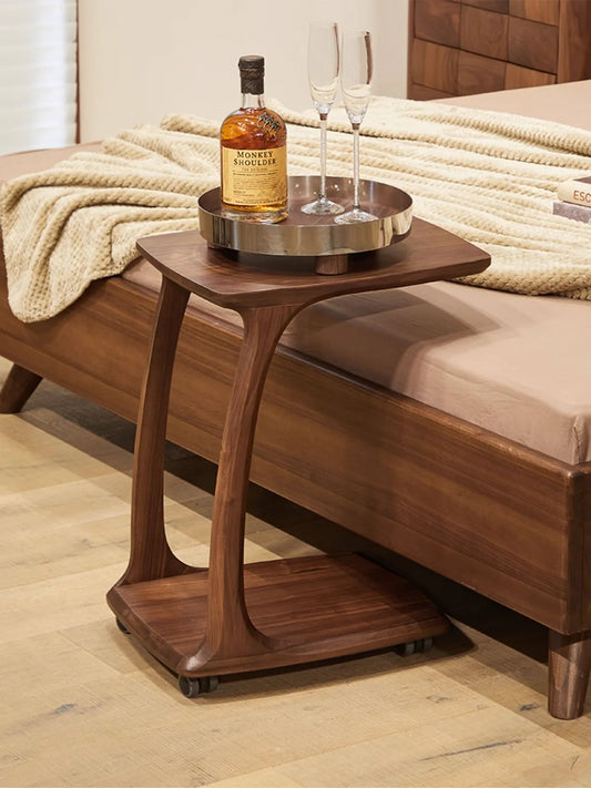 The Helios rolling C-table with hidden caster wheels, used as a stylish and mobile bedside table holding a whiskey tray.