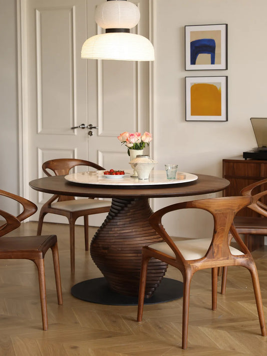 The Helios Round Dining Table styled in an elegant dining room with matching walnut curved chairs, a floral centerpiece, and a record player console.