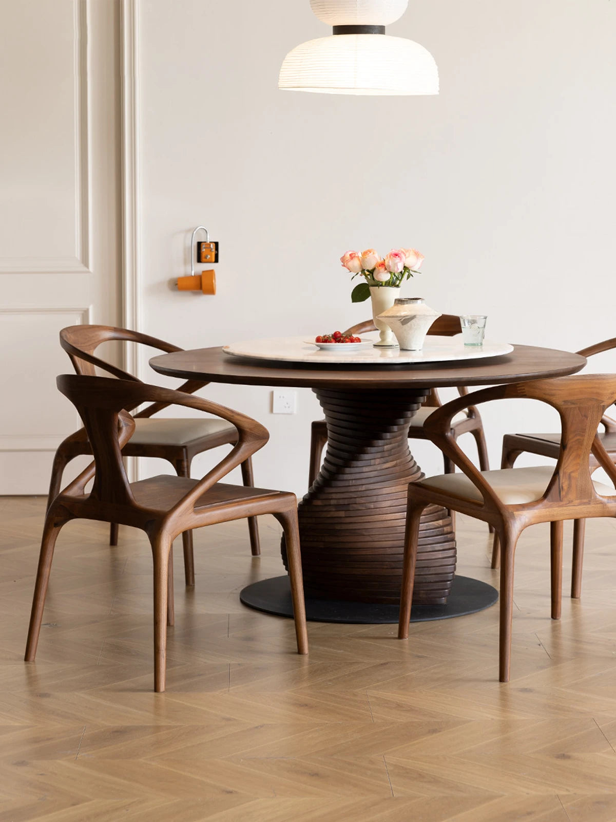 Walnutry Helios solid walnut dining chairs arranged around a sculptural round table in a modern, minimalist dining room.