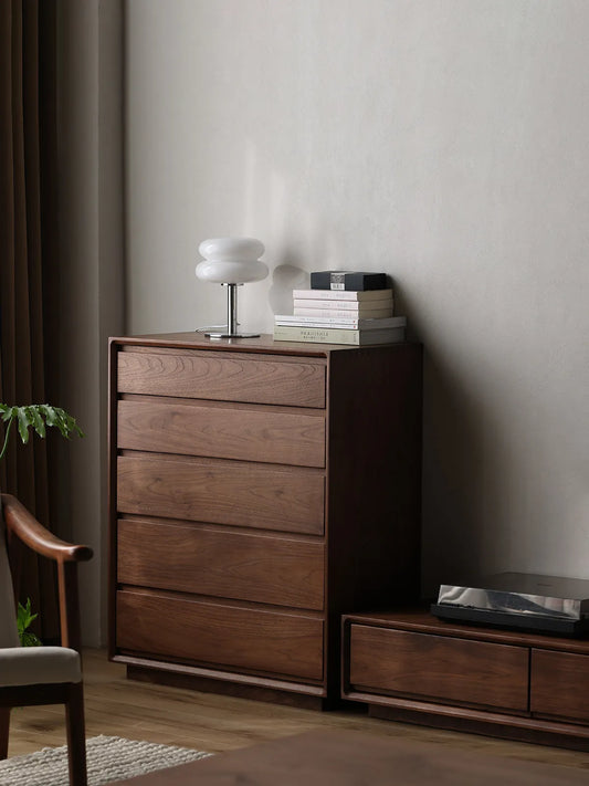 Angled view of The Heritage 5-Drawer Tallboy dresser next to a matching walnut lowboy in a minimalist, naturally lit room.