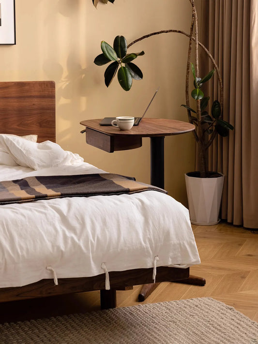 The Heritage Adjustable Side Table styled as a convenient over-bed table in a cozy bedroom, holding a laptop and a coffee mug.