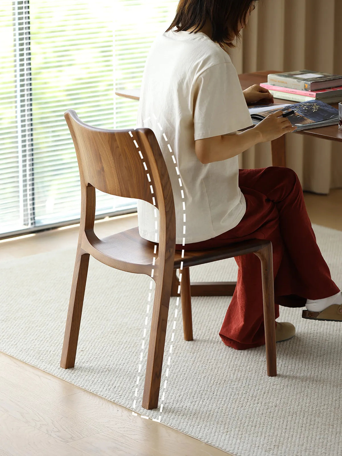 A woman reading at a desk while seated in The Heritage Dining Chair, demonstrating the reliable lumbar support of the curved wooden backrest.