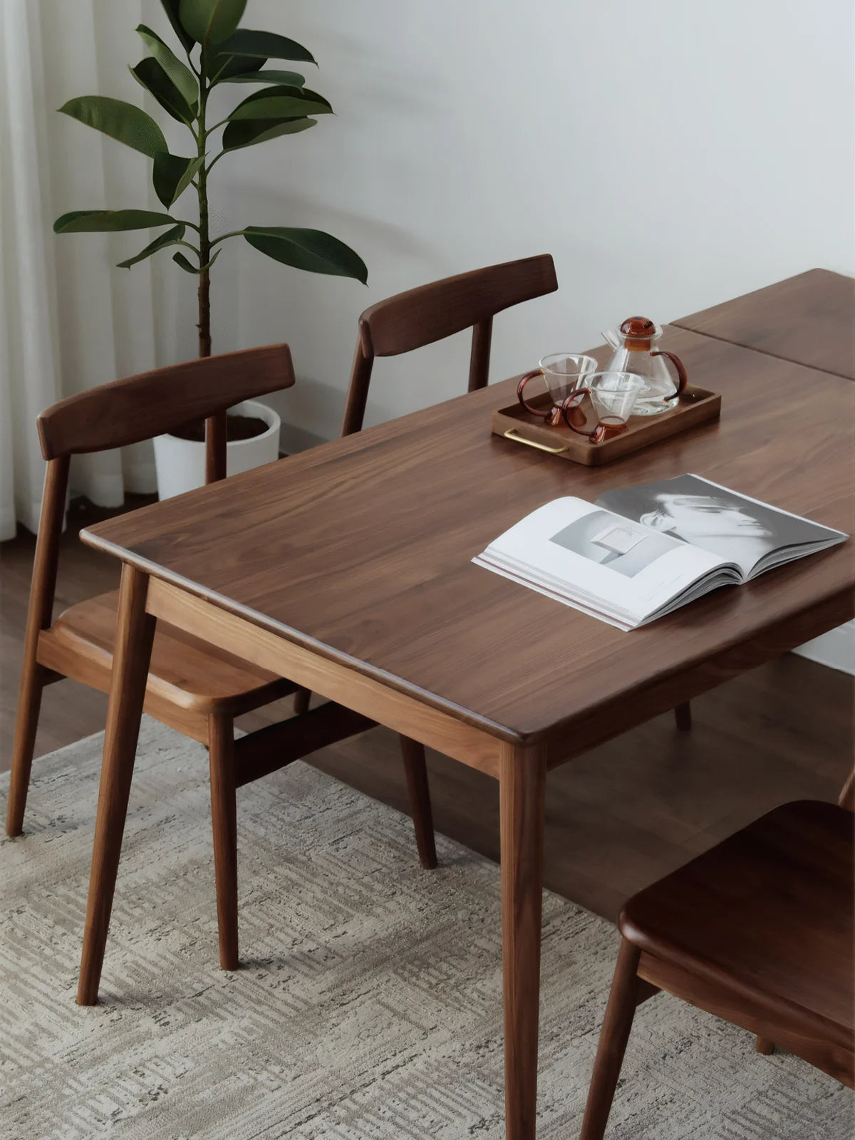 Rectangular extendable dining table in solid walnut shown with sculpted chairs in a bright minimalist dining room