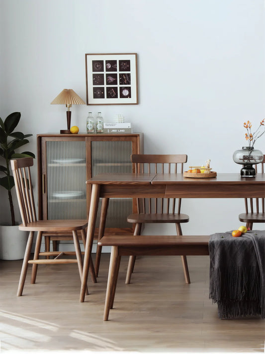 Side perspective of a rectangular solid wood extendable dining table in American black walnut with matching bench and chairs